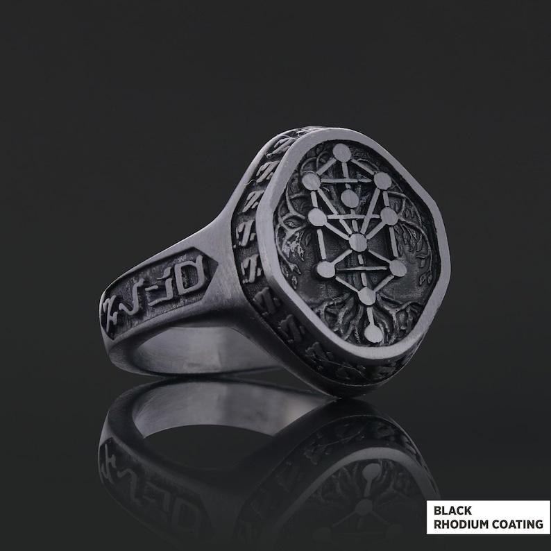 Op de afbeelding: Een zilverkleurige ring met een gedetailleerd ontwerp. De ring heeft een gegraveerd geometrisch patroon op de voorkant en zijkanten. De tekst "BLACK RHODIUM COATING" is rechtsonder zichtbaar.
