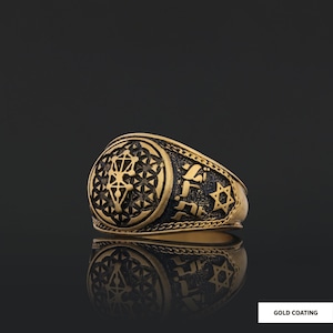 Op de afbeelding: Een gouden ring met een zwart emaille ontwerp met een geometrisch patroon, Hebreeuwse tekst en een Davidster. De ring heeft een brede band en een verhoogd ontwerp.