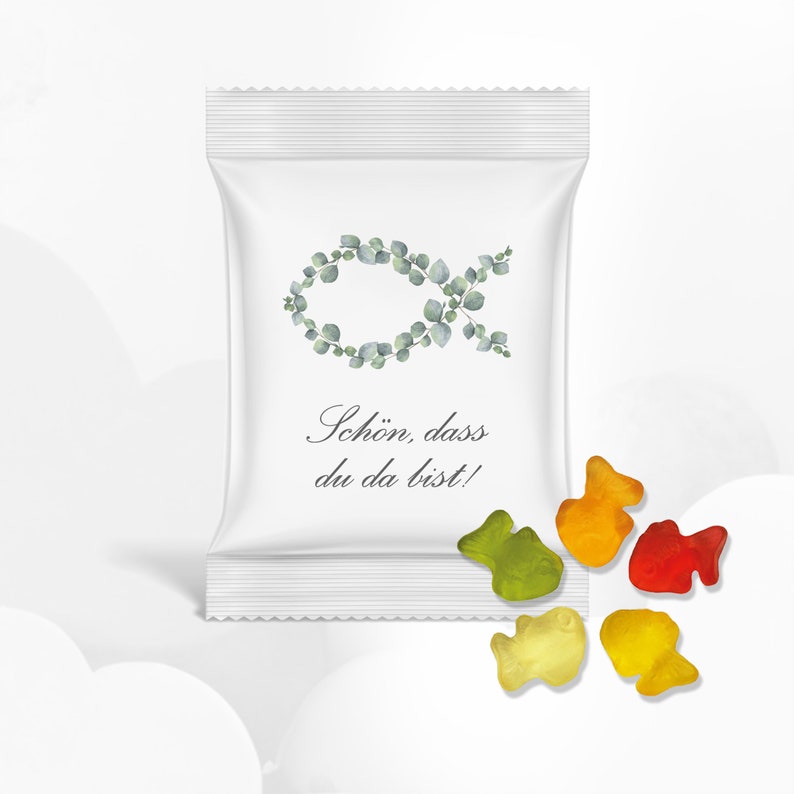 Puede incluir: Una bolsa blanca con un dise&ntilde;o de pez verde frondoso y el texto "Sch&ouml;n, dass du da bist!" La bolsa est&aacute; abierta y hay cinco peces gomosos de colores sobre una superficie blanca.