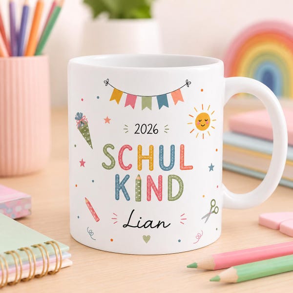 Pode incluir: Uma caneca de cerâmica branca com o texto 2026 SCHUL KIND e o nome Lian em letra cursiva preta. O design inclui ilustrações coloridas de bandeirolas, um sol, um lápis, um cone escolar e tesouras, tudo numa fonte com estilo de costura.