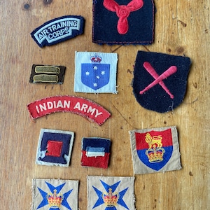 May include: A collection of vintage military badges, including the Air Training Corps, Indian Army, and Royal Air Force. The badges are made of felt and embroidered with various colours, including red, blue, and white.