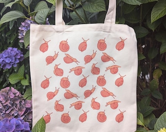 Puede incluir: Una bolsa de lona blanca con un patrón repetido de caracoles rosas. Los caracoles están todos mirando en la misma dirección y están dispuestos en un patrón de cuadrícula.
