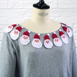 May include: A grey sweater with a crocheted trim of Santa Claus faces around the neckline. The trim is white and red with black eyes and a white beard.