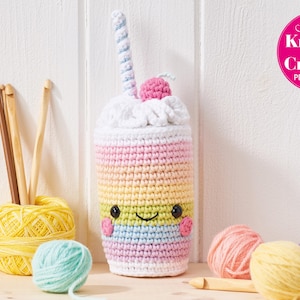 Puede incluir: Un recipiente en forma de batido de leche tejido a ganchillo en colores pastel, con una cara sonriente, una cereza y una pajita a rayas. La imagen incluye ovillos de lana, ganchillos y el texto "Simply Knitting & Crochet PDF Patterns".