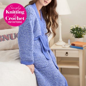 May include: A periwinkle blue crochet robe featuring long sleeves, a V-neckline, a matching tie belt at the waist, and two front pockets. The garment has a textured stitch pattern and a solid blue border along the cuffs and front opening edges.