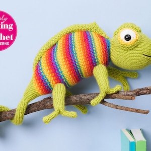 Op de afbeelding: Een gehaakte kameleon met een regenboogkleurig gestreept lichaam, zittend op een tak. De kameleon heeft een groen lichaam en een wit oog. De tekst "Simply Knitting & Crochet PDF Patterns" staat in een roze cirkel in de linkerbovenhoek van de afbeelding.