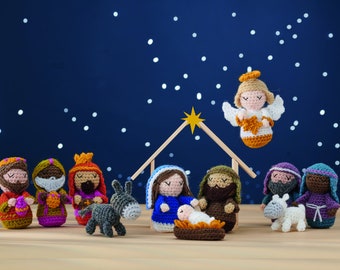 May include: A crocheted nativity scene with a star, angel, and figures of Mary, Joseph, baby Jesus, a donkey, a sheep, and three wise men. The scene is set against a dark blue background with white dots.