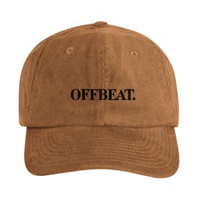 May include: A brown corduroy baseball cap featuring the word OFFBEAT. embroidered in black thread across the front centre. The cap has a structured crown, a curved brim with visible stitching, and a button at the top of the dome.