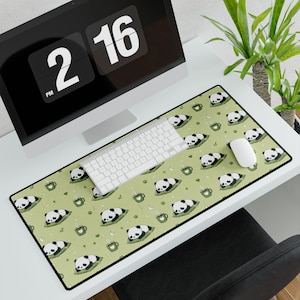 May include: A rectangular desk mat featuring a repeating pattern of sleeping pandas on green cushions, interspersed with green mugs, small stars, and crescent moons against a light sage green background with a black border trim.