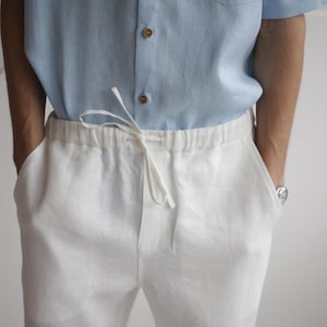 Man wearing FLORIDA white linen pants, featuring a comfortable elastic waistband and pockets, styled for a relaxed yet smart summer look.