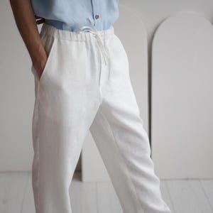 Side view of men's white linen pants with pockets and adjustable waistband, demonstrating the relaxed yet sophisticated fit.