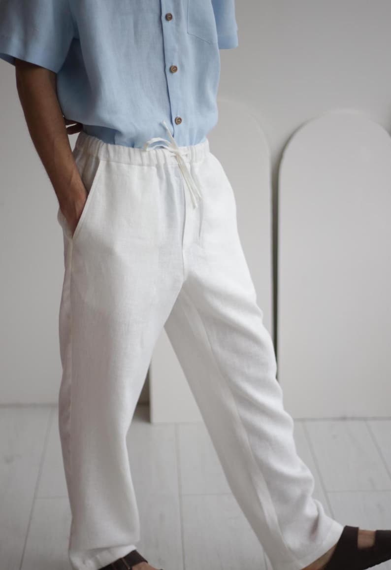 Side view of men's white linen pants with pockets and adjustable waistband, demonstrating the relaxed yet sophisticated fit.