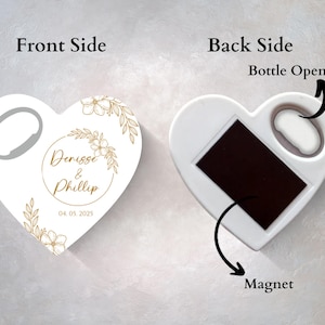 Może przedstawiać: Biały otwieracz do butelek w kształcie serca z magnesem z tyłu. Przednia strona zawiera złoty wz&oacute;r kwiatowy i tekst "Denise & Phillip 04.05.2025".