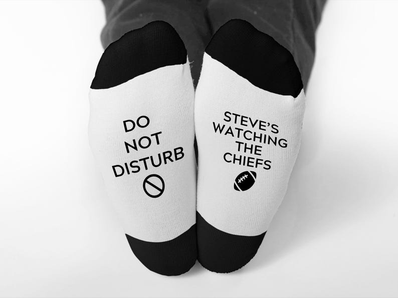 May include: A pair of white socks with black heels and toes. One sock reads "DO NOT DISTURB" with a no-entry symbol. The other sock says "STEVE'S WATCHING THE CHIEFS" with a football graphic.