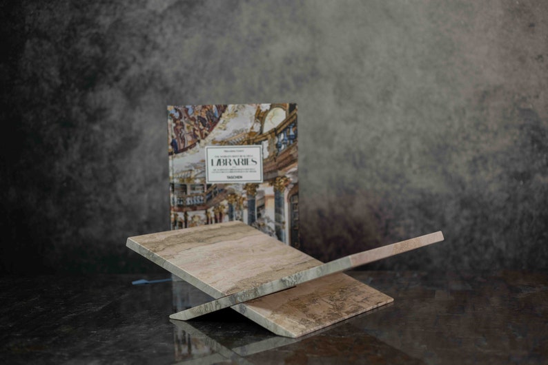 K&ouml;nnte beinhalten: Ein Buch mit dem Titel "Labyrinth" mit einem farbenfrohen Bild eines Geb&auml;udes auf dem Cover wird auf einem hellbraunen Holzbuchst&auml;nder pr&auml;sentiert. Der St&auml;nder besteht aus zwei Holzst&uuml;cken, die im Winkel gekreuzt sind.