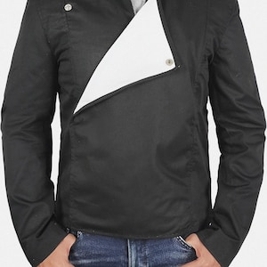 May include: Black jacket with a white asymmetrical panel. The jacket has a stand-up collar, long sleeves, and a button closure. The model is wearing blue jeans.