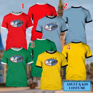 May include: A collection of colorful t-shirts with the "Disney Games" logo. The shirts are red, light blue, green, and yellow, with contrasting trim. The text "ADULT & KID COSTUME" is displayed on a blue rectangle.