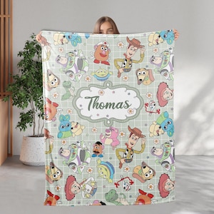 May include: A green and white blanket with a grid pattern and a variety of Toy Story characters, including Woody, Buzz Lightyear, and Mr. Potato Head. The blanket is personalized with the name "Thomas".
