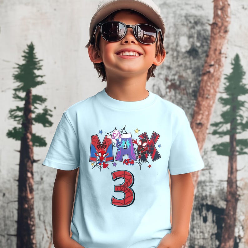 Pode incluir: Camiseta azul claro com um gr&aacute;fico de personagens do Homem-Aranha que soletram o nome "MAX" e o n&uacute;mero "3" em vermelho.