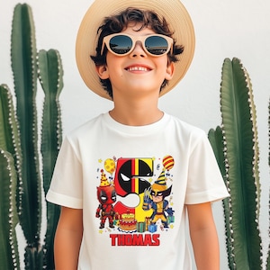 May include: White t-shirt with a red and black Deadpool and Wolverine graphic. The graphic includes a number 5, party hats, and presents. The text "THOMAS" is printed below the graphic.