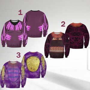 Op de afbeelding: Drie paarse sweatshirts met unieke ontwerpen. E&eacute;n heeft een zwarte V-hals en neonroze bliksemgraphics. Een andere heeft een bruin en bordeauxrood stammenpatroon. De derde heeft een gouden schildontwerp.