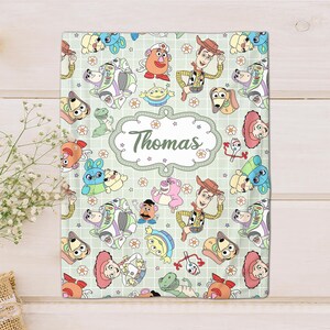 May include: A green and white blanket with a repeating pattern of Toy Story characters, including Woody, Buzz Lightyear, and Mr. Potato Head. The blanket has a personalized name, "Thomas", in a decorative font.