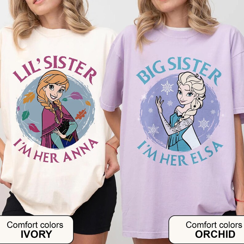 May include: Two t-shirts, one ivory and one orchid, featuring cartoon characters. The ivory shirt says "Lil' Sister, I'm Her Anna" with a picture of Anna. The orchid shirt says "Big Sister, I'm Her Elsa" with a picture of Elsa.