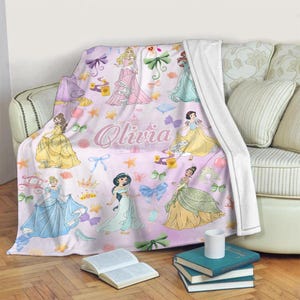 May include: Pink fleece blanket with a princess theme. The blanket features various Disney princesses, including Cinderella, Snow White, Belle, and Ariel. The blanket also has a pink castle and the name "Olivia" printed on it.