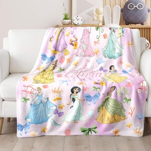 May include: A pink fleece blanket with a pattern of Disney princesses, including Cinderella, Belle, Jasmine, and Snow White. The blanket also features crowns, stars, bows, and the name "Olivia".