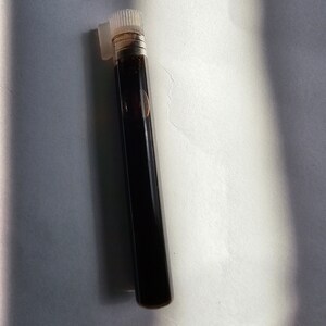 May include: A small, clear glass bottle with a black liquid inside and a white plastic cap.