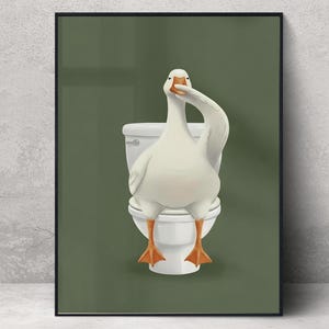 May include: A framed art print featuring a white goose sitting on a toilet, with its neck arched. The background is a solid olive green. The artwork is displayed in a bathroom setting with a wooden ladder and a woven basket.