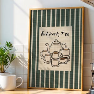 May include: A framed wall art print featuring a dark green and white vertical striped background with a central cream-colored rectangle. The print displays a black line drawing of a teapot and several teacups with the text But first, Tea.