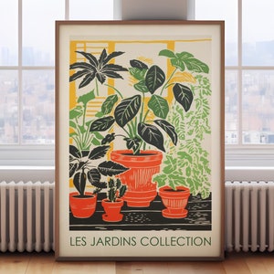 May include: A framed art print with a botanical illustration of potted plants. The artwork uses green, orange, and black against a cream background. The text "LES JARDINS COLLECTION" is at the bottom. The print is displayed in a room with a window.