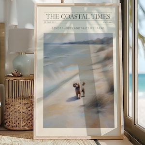Peut inclure: Impression encadrée intitulée "The Coastal Times" représentant une scène de plage avec un petit chien. L'impression comprend le texte "Sandy Shores and Salty Wet Paws" et la date "28 juillet 2011". L'œuvre est encadrée dans un cadre en bois clair.