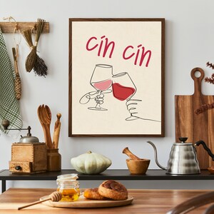 May include: A beige framed print with a line drawing of two wine glasses clinking. The text "cin cin" is written in red above the glasses.
