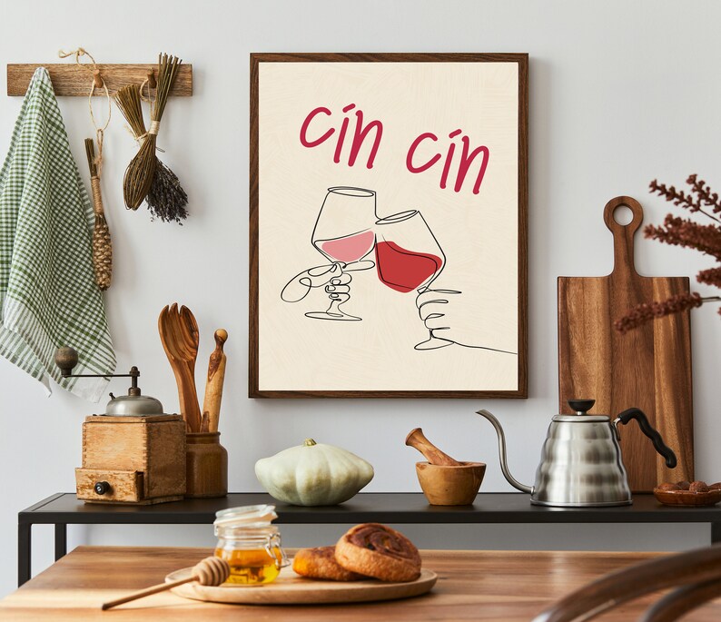 May include: A beige framed print with a line drawing of two wine glasses clinking. The text "cin cin" is written in red above the glasses.