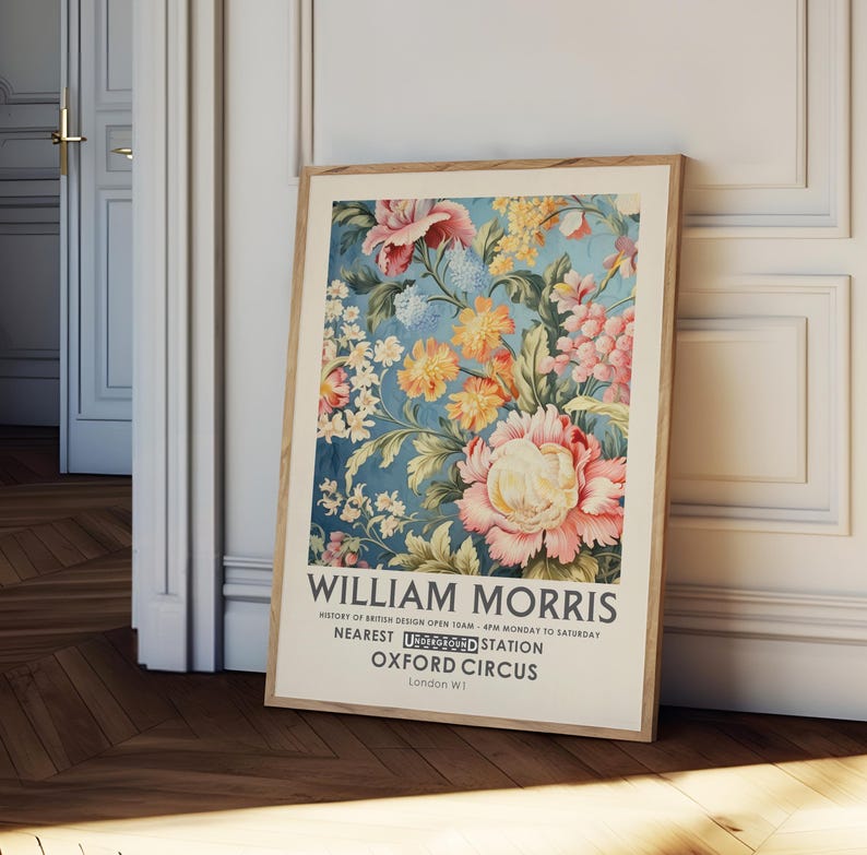 May include: A vintage poster featuring a floral design by William Morris. The poster is in a wooden frame and has a blue background with pink, yellow, and white flowers. The text on the poster reads "William Morris, History of British Design Open 10AM - 4PM Monday to Saturday, Nearest Underground Station Oxford Circus, London W1."
