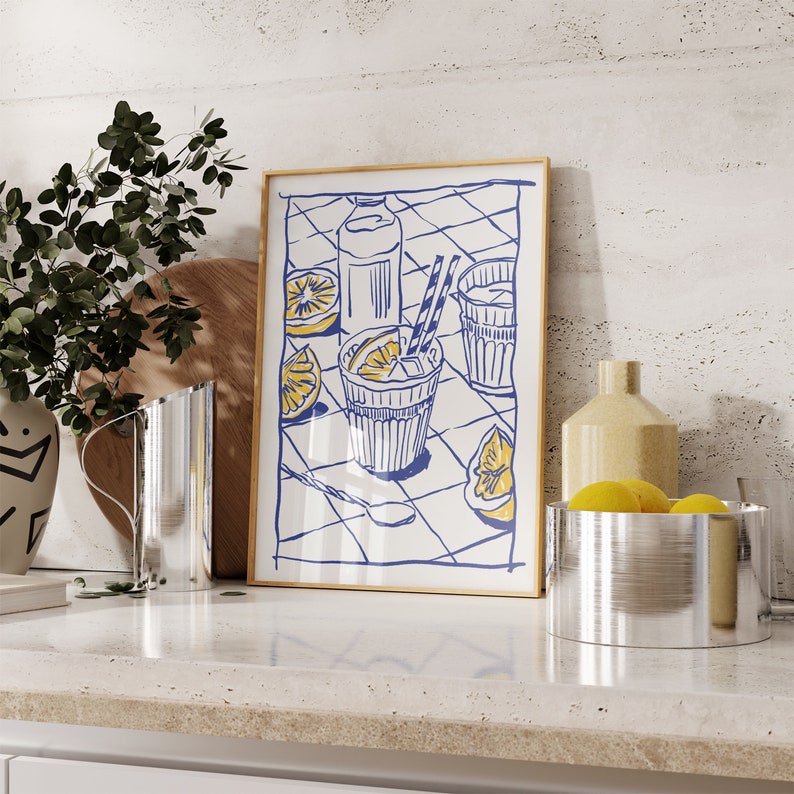 Pu&ograve; includere: Una stampa artistica incorniciata con un'illustrazione a tema limone in blu e giallo. L'opera raffigura un bicchiere di limonata con una cannuccia, fette di limone e una bottiglia su uno sfondo a scacchi. La stampa &egrave; esposta su un piano di lavoro con altri oggetti da cucina.