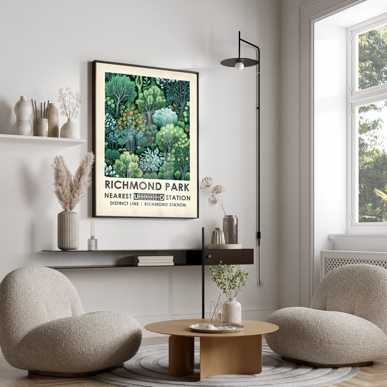 Op de afbeelding: Een ingelijste poster met een groene en witte illustratie van bomen en de tekst "Richmond Park Nearest Underground Station District Line | Richmond Station". De poster hangt aan een witte muur in een woonkamer met twee fauteuils en een salontafel.