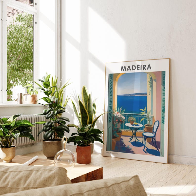 May include: A vintage travel poster with the word "MADEIRA" in bold white letters on a blue background. The poster depicts a balcony overlooking a blue ocean with a table and chairs on the balcony. The balcony is surrounded by lush green plants.