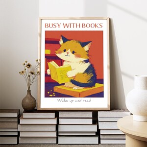 May include: A framed illustration of a cat reading a book. The cat is sitting on a stack of books. The text on the image reads "Busy with Books" and "Wake up and read".
