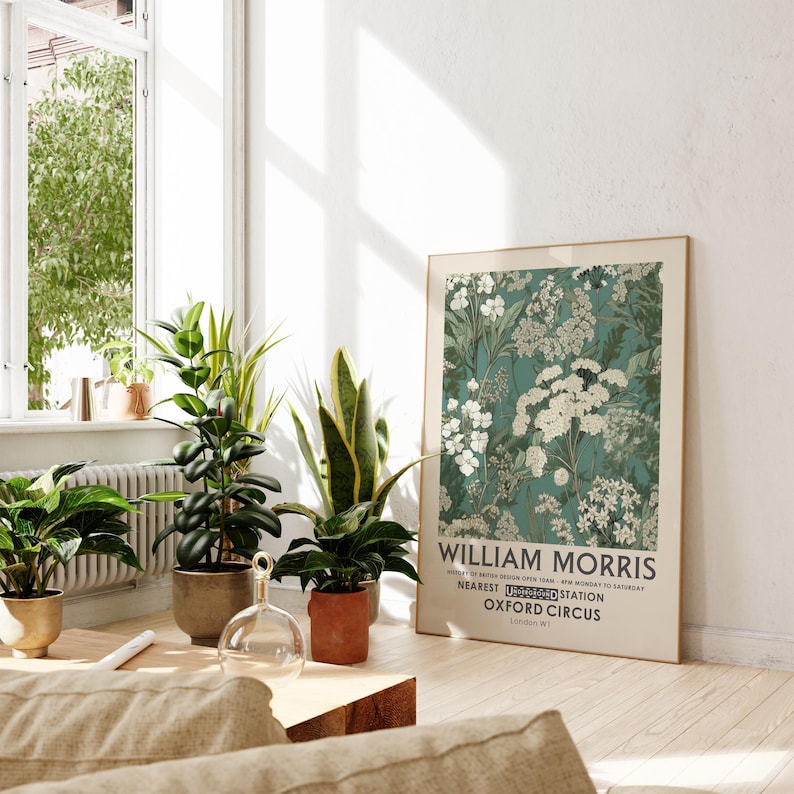 May include: A framed William Morris art print featuring a teal floral pattern with white flowers. The print is displayed in a bright room with potted plants and a wooden coffee table. The text on the print reads "William Morris" and "Oxford Circus".