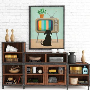 May include: A rustic wooden shelf unit with six shelves, featuring a black metal frame and glass doors. The shelves are filled with various items, including books, decorative bowls, and a small potted plant. A framed print of a dog watching a vintage television set hangs above the shelf unit.
