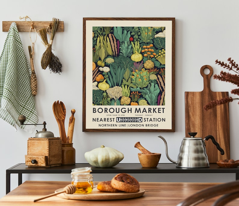 Puede incluir: Un p&oacute;ster enmarcado con un borde marr&oacute;n oscuro presenta una colorida ilustraci&oacute;n de varias verduras. El p&oacute;ster dice "BOROUGH MARKET" con el horario y la estaci&oacute;n de metro m&aacute;s cercana. El p&oacute;ster se muestra en un entorno de cocina con utensilios de madera y un molinillo de caf&eacute;.