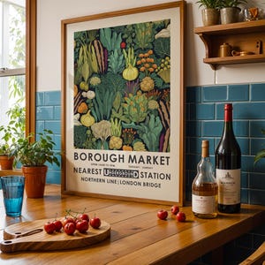 Puede incluir: Un p&oacute;ster enmarcado del mercado de Borough con una colorida ilustraci&oacute;n de verduras. Una tabla de cortar de madera con cerezas, un vaso de agua y botellas de vino est&aacute;n sobre una mesa de madera. Hay plantas en una estanter&iacute;a.
