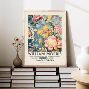 May include: A vintage poster featuring a floral design with pink, yellow, and white flowers on a blue background. The poster has the text "WILLIAM MORRIS" at the top and "HISTORY OF BRITISH DESIGN OPEN 10AM-4PM MONDAY TO SATURDAY" below the floral design. The poster also includes the text "NEAREST UNDERGROUND STATION OXFORD CIRCUS London WI".