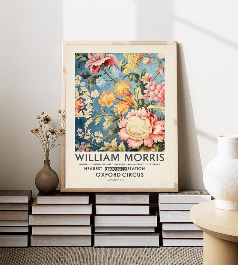 May include: A vintage poster featuring a floral design with pink, yellow, and white flowers on a blue background. The poster has the text "WILLIAM MORRIS" at the top and "HISTORY OF BRITISH DESIGN OPEN 10AM-4PM MONDAY TO SATURDAY" below the floral design. The poster also includes the text "NEAREST UNDERGROUND STATION OXFORD CIRCUS London WI".