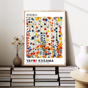 May include: A framed print of an abstract painting by Yayoi Kusama. The painting features a white background with colorful circles and lines in shades of blue, red, yellow, and orange. The title of the painting is "草間彌生" and the text "Yayoi Kusama" and "Mori Museum Tokyo 1985" are printed below the painting.
