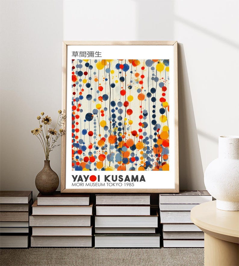 May include: A framed print of an abstract painting by Yayoi Kusama. The painting features a white background with colorful circles and lines in shades of blue, red, yellow, and orange. The title of the painting is "草間彌生" and the text "Yayoi Kusama" and "Mori Museum Tokyo 1985" are printed below the painting.