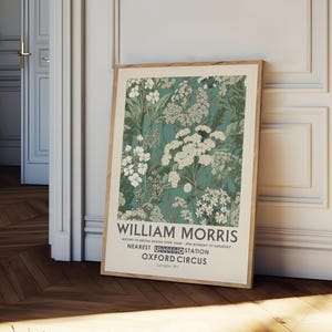May include: A framed art print featuring a floral design in shades of teal, green, and white. The print includes the text "WILLIAM MORRIS" and other text about the history of British design and the Oxford Circus station.